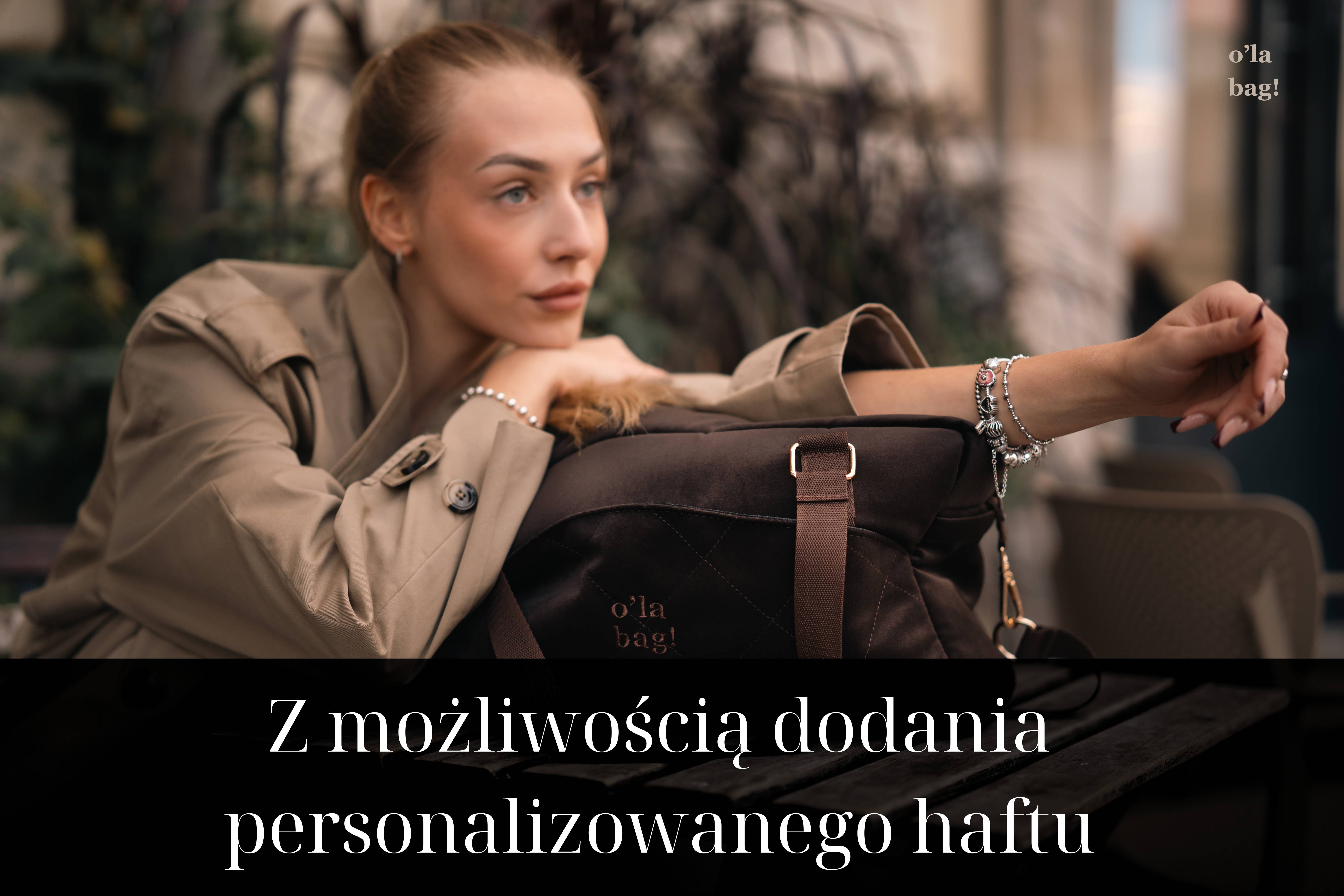 Brązowa, pikowana torba o'la bag! z welurowo-zamszowej tkaniny, leżąca na ławce obok kobiety w beżowym trenczu. Hasło: Z możliwością dodania personalizowanego haftu