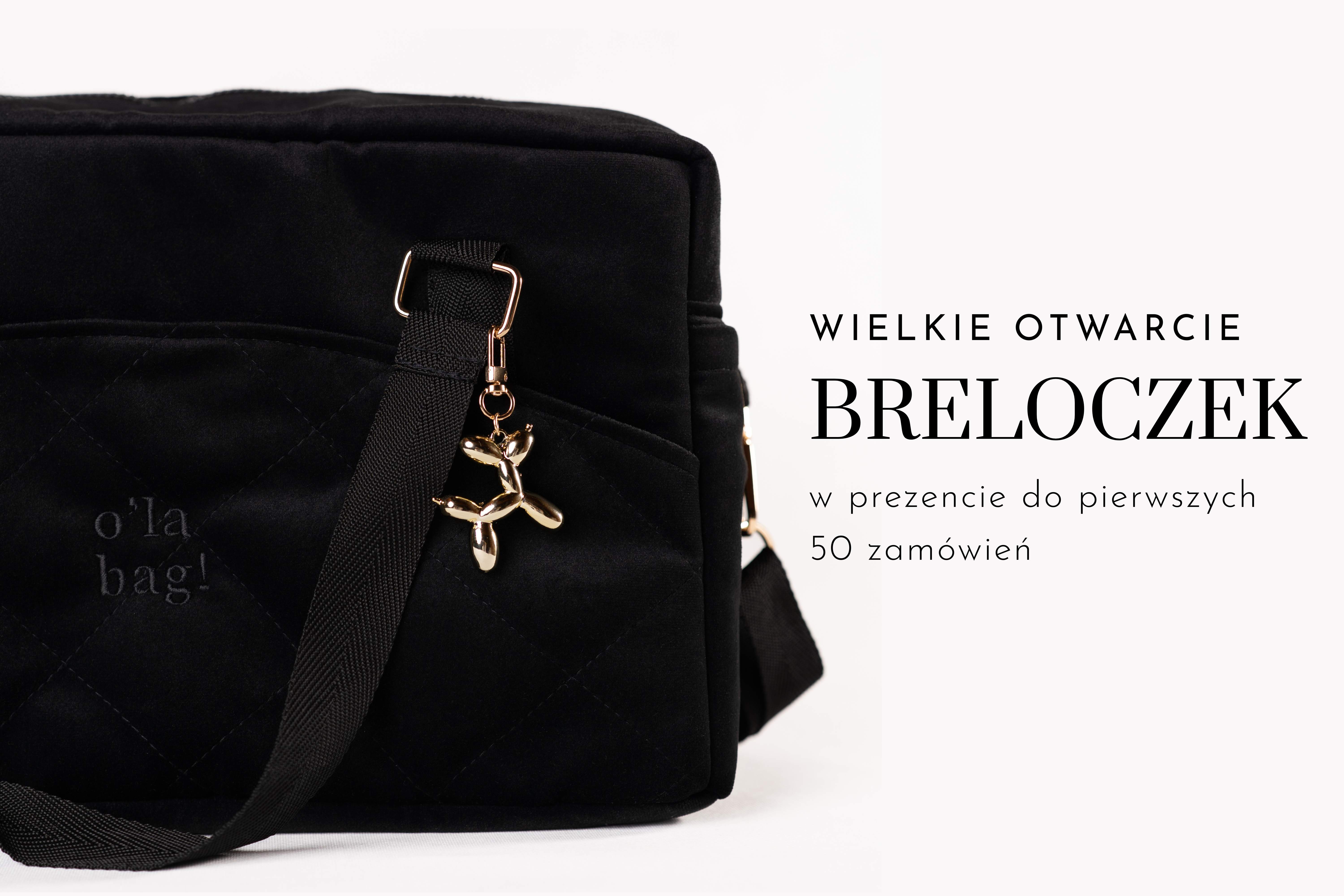 Torba o'la bag! z zawieszonym złotym brelokiem w kształcie balonowego pieska, pokazana z napisem „Brelok w prezencie”.